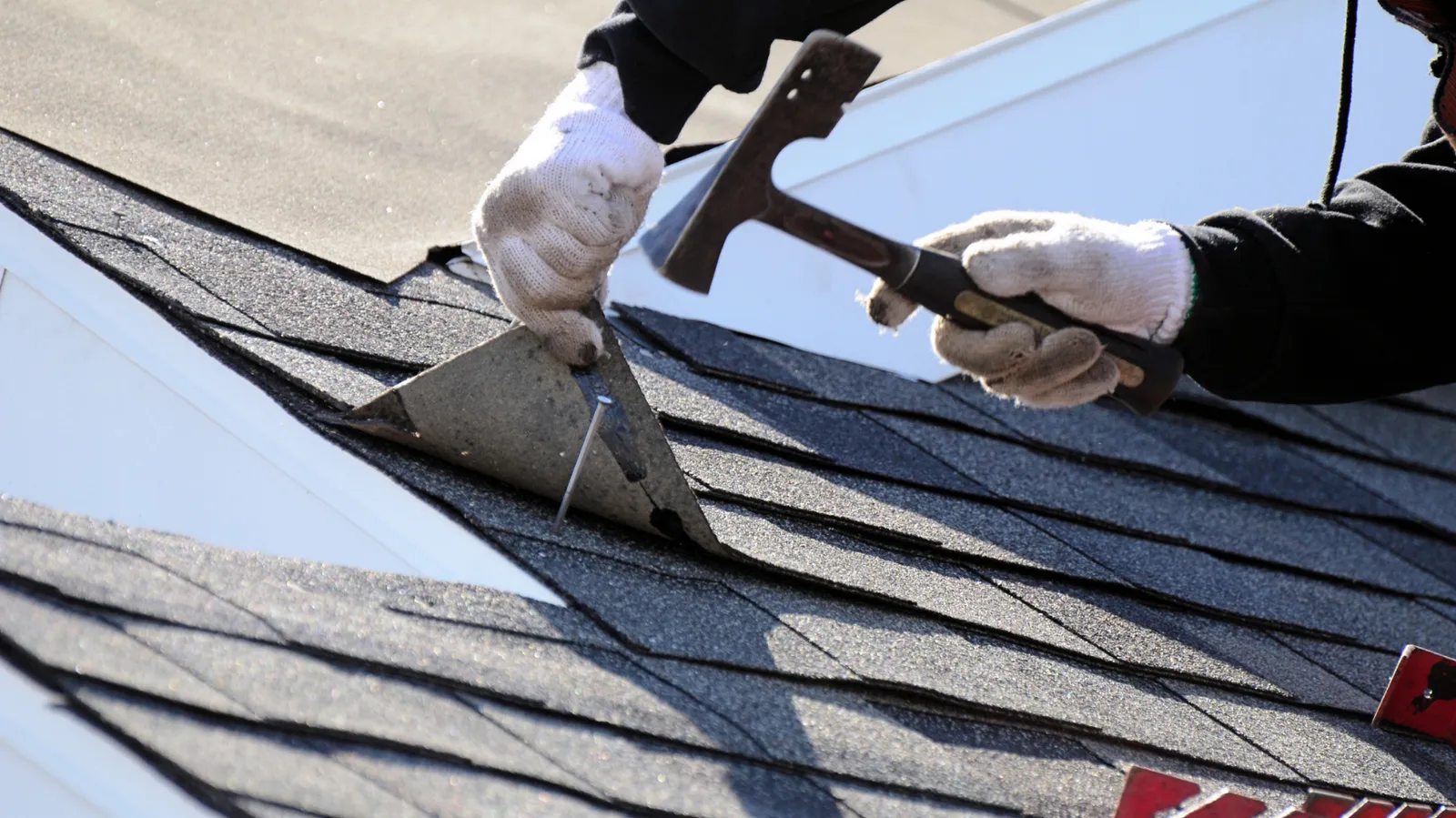 Gloved roofer nailing metal flashing onto shingles with a roofing hammer